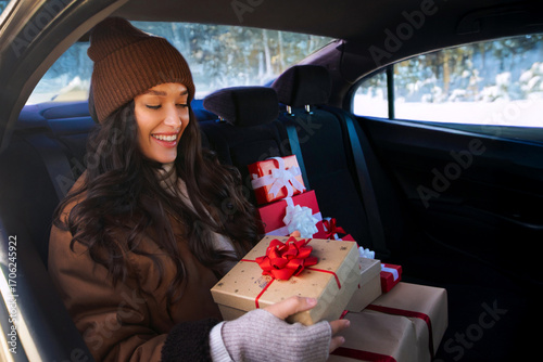 Excited lady sitting on back seat of car with gift boxes, preparing for Christmas holidays and enjoying festive winter mood