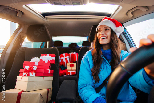 Happy woman driver in Santa hat delivering Xmas gift boxes, feeling enjoyment of winter holidays and festive mood