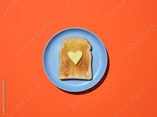 A slice of toast on blue plate with a heart shaped piece of butter on 