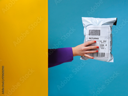 Woman’s hand holding parcel from behind yellow wall.