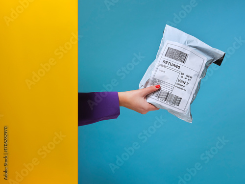Woman’s hand holding parcel from behind yellow wall.