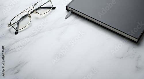 Gray marbled surface with right corner with closed notebook, left corner with glasses, clean center
