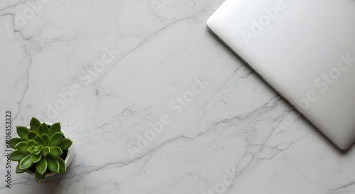 Gray marbled surface with right corner with closed laptop, left corner with succulent plant, clean center