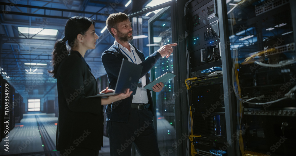 © Aleksei Gorodenkov/Stocksy - Two technicians talk, use laptop and work in data center.