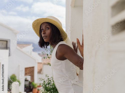 Model Posing in Stylish Hat Against White Buildings in Sunny Location