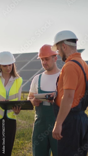 Engineers in hard hats discuss plans at a solar panel installation site, vertical video.