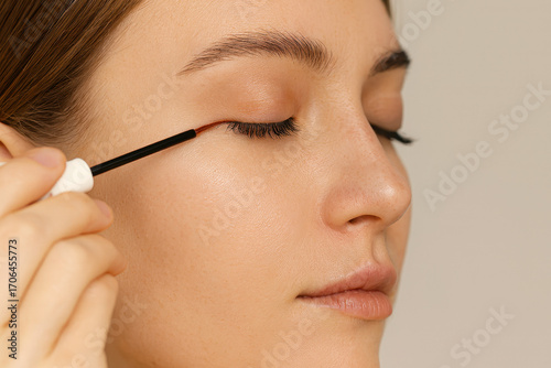 Young woman with closed eyes carefully applying eyelash growth serum along the lash line with a brush. Eyelash care, close-up, beauty routine at home.