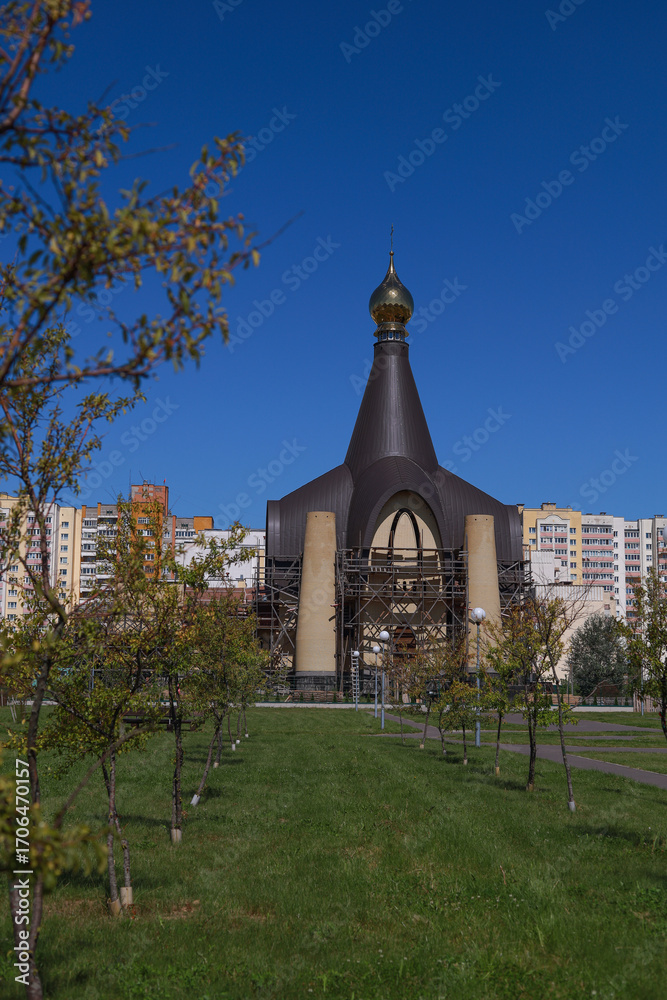 Fototapeta premium Orthodox church with scaffolding, golden dome and unfinished facade against blue sky, religious architecture in progress with copy space.