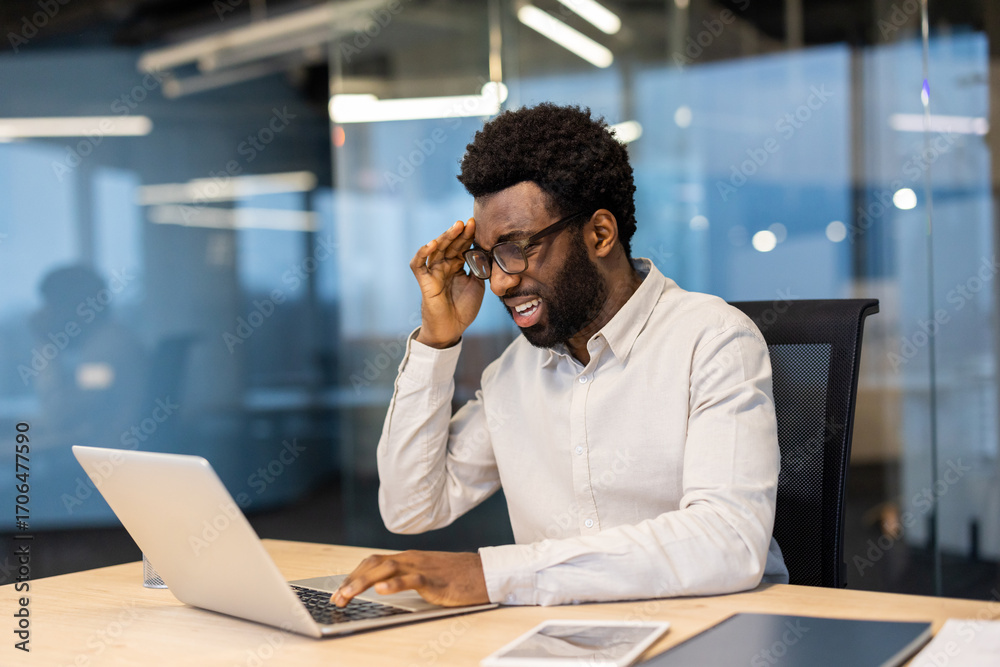 Obraz premium Stressed businessman having headache while working on laptop in office