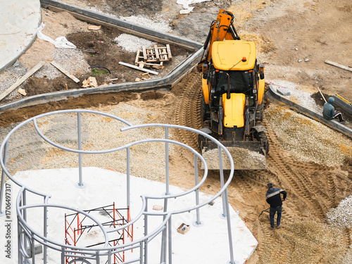 Excavator and workers building playground area at construction site
