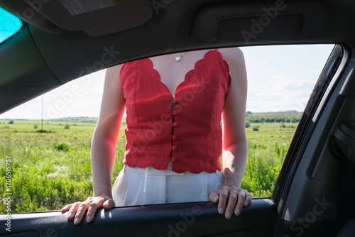 Woman in red top stands by car in a vibrant green landscape