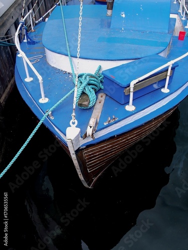 Close-up view of a small wooden boat with blue deck, moored at the pier with ropes and anchor visible.
