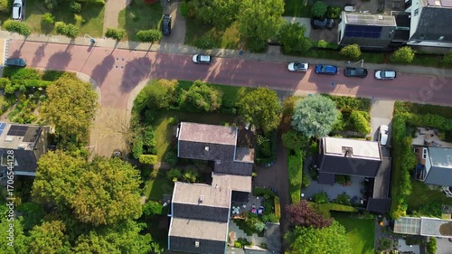 Aerial view of a planned residential neighborhood with dark-roofed houses, gardens, patios, and tree-lined paths. The layout integrates private outdoor spaces with natural greenery.