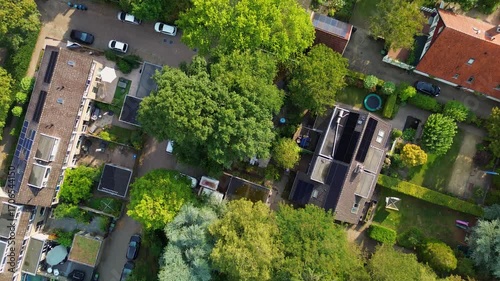 Aerial view of a planned residential neighborhood with dark-roofed houses, gardens, patios, and tree-lined paths. The layout integrates private outdoor spaces with natural greenery.