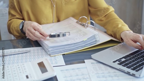 Photography Female auditor in business attire inspecting financial reports with magnifying glass, surrounded by documents and a laptop and calculator