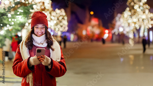 Vászonkép Young woman using smartphone while walking in the evening on Xmas Eve, enjoying