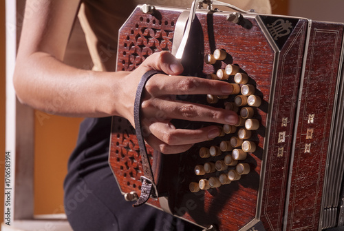 Close-up of a musician’s hand playing a vintage bandoneon, highlighting the wooden body, pearl buttons, and warm textures that embody the essence of tango tradition.