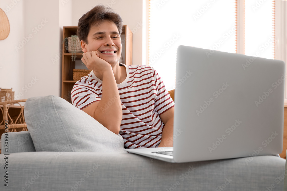 Fototapeta premium Young man video chatting with laptop on sofa at home