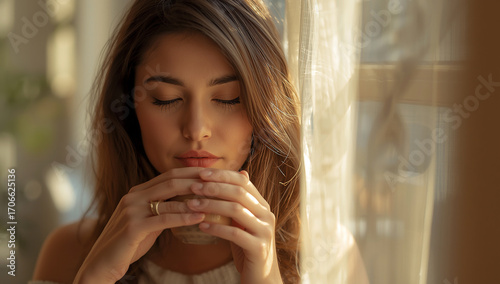 A serene young woman enjoys a moment of tranquil reflection, gently holding a warm beverage as soft, natural sunlight illuminates her face, creating a cozy and peaceful morning scene