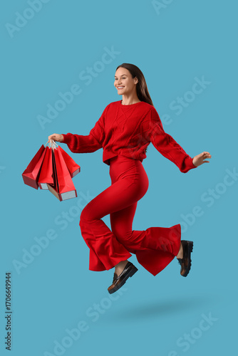 Young happy stylish woman with shopping bags jumping on blue background