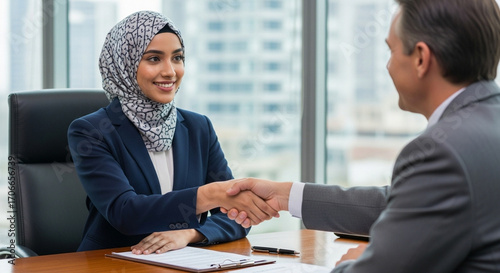Fototapeta Naklejka Na Ścianę i Meble -  Young muslim bank worker woman in hijab shaking hand with client, hr manager welcome recruit employee. Middle eastern arab businesswoman showing greeting after signing contract with business partner
