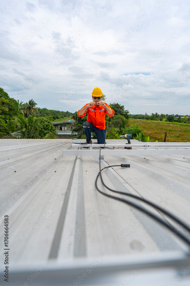Obraz premium Technician in safety uniform and helmet kneeling on a rooftop, using a drill for precise installation work. A scene highlighting safety, professionalism, and technical expertise in construction.