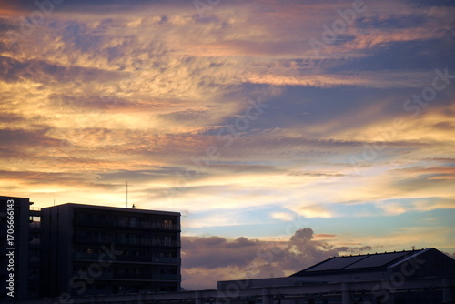 夕暮れの空に広がるオレンジ色の雲と、シルエットになった建物が写っています。雲の層が重なり合い、美しいグラデーションを描いています。