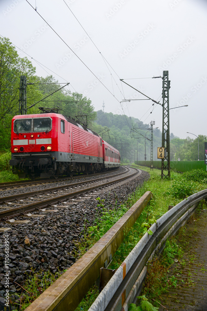 Naklejka premium Red Electric Train Traveling Through Green Forest Landscape