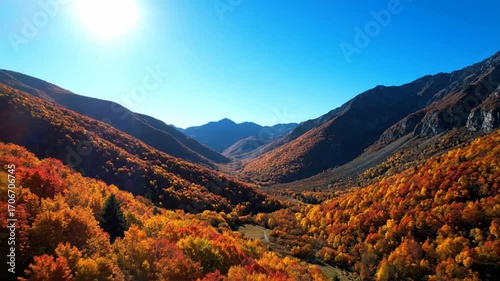 Aerial footage of a pristine, remote mountain range covered in autumn colors under a bright, sunny sky backdrop, wilderness, nature