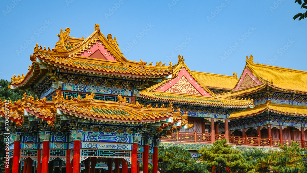Naklejka premium Traditional Chinese temple in Penglai, Shandong, with red pillars, golden roofs, and ornate details, surrounded by lush greenery and a serene natural setting.