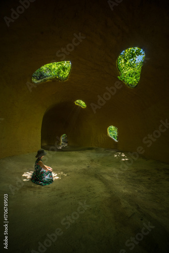 Woman in Hat Sitting Inside Underground Cave Dwelling with Natural Skylights and Tunnel