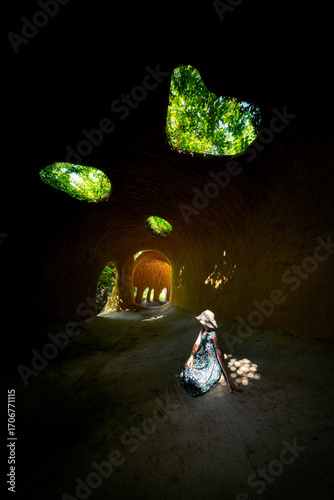 Woman in Hat Sitting Inside Underground Cave Dwelling with Natural Skylights and Tunnel