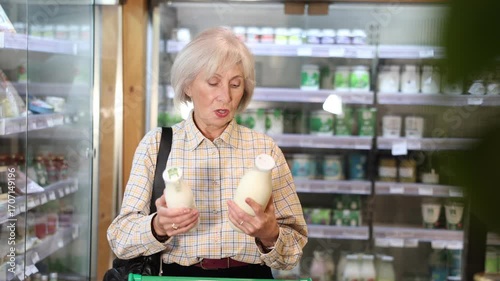 Young woman buyer chooses milk in bottle in eco grocery supermarket