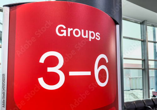 A bold red airport departure gate sign welcomes passengers in boarding groups 3 to 6.