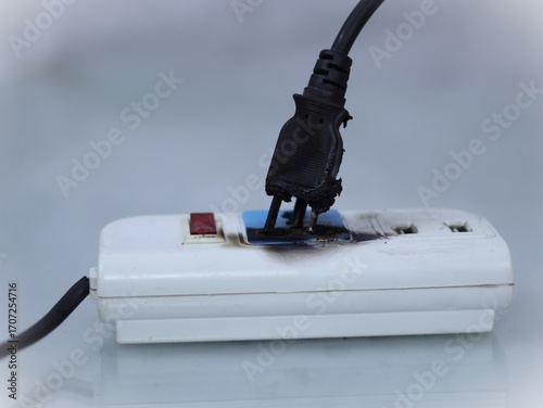 Fotografija This image depicts an electrical hazard, likely caused by an overloaded or faulty power strip and plug