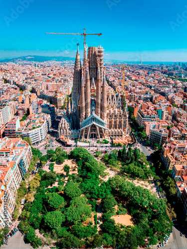 Photography Aerial view of Barcelona with the Sagrada Familia, city buildings, park, and sea skyline in the distance on a sunny day