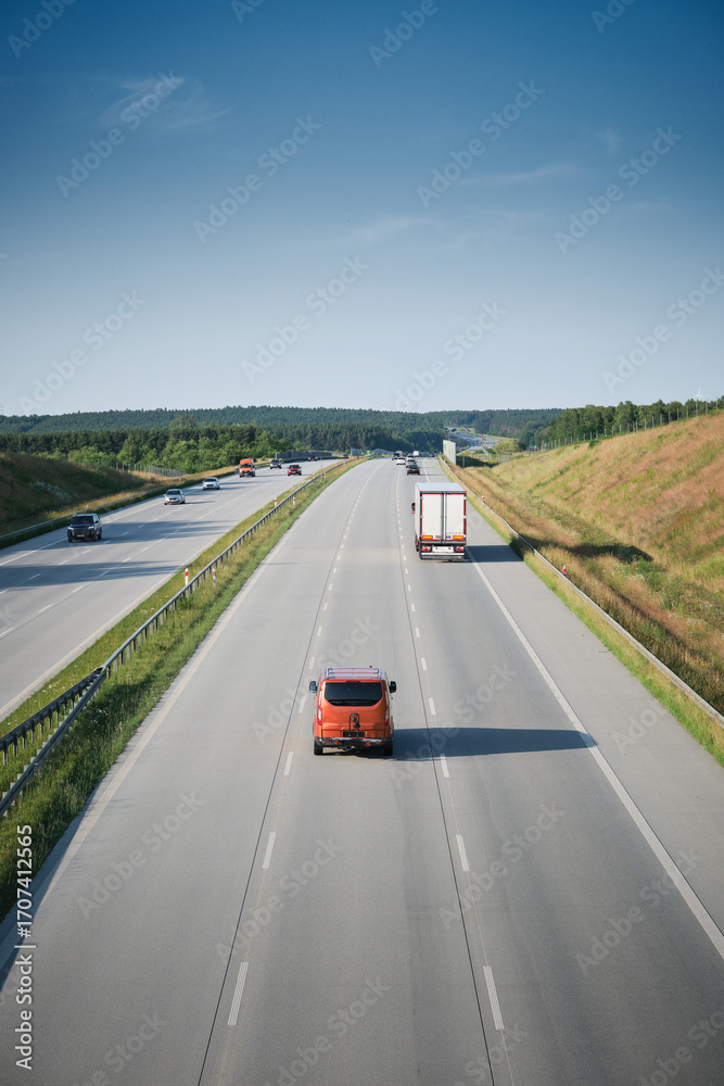 Fototapeta premium Scenic view of highway traffic with cars and trucks under clear blue sky, symbol of transport and travel.