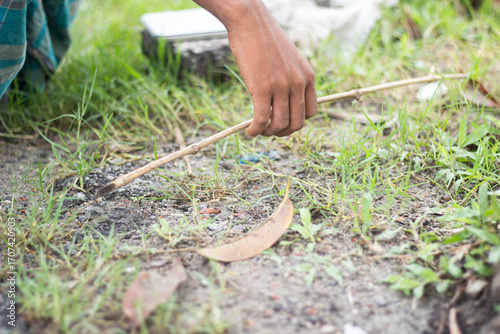 A persons hand holding a thin stick over the ground