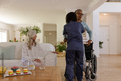 Caregiver assisting senior African American man from wheelchair while friend watches