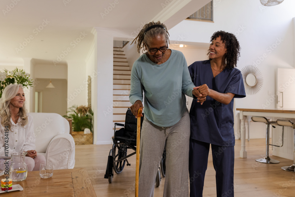 Fototapeta premium African American woman using cane walking with caregiver at home, smiling together