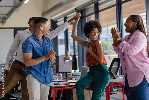 Colleagues celebrating success with high fives in modern office setting