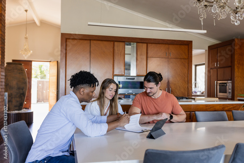 Diverse friends discussing project at home, using tablet and notebook on table
