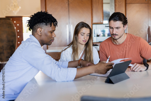 Diverse friends collaborating on project with tablet and documents at home
