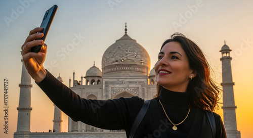 Happy female traveler taking a beautiful selfie with a famous Indian mausoleum in the background during a golden sunset