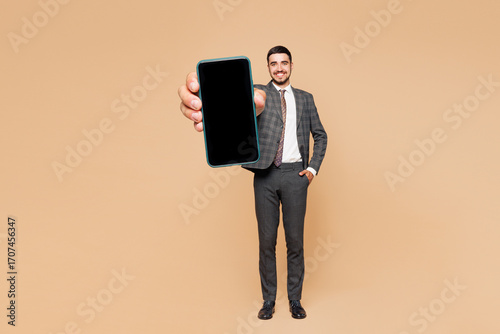 Full body young employee business man corporate lawyer wear classic formal grey suit shirt tie work in office hold in hand use blank screen mobile cell phone isolated on plain beige background studio.