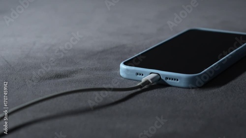 A mobile phone in a blue case is charging.
The smartphone is charging from a wall outlet using a power cord.
A power cord connected to the smartphone provides fast charging.