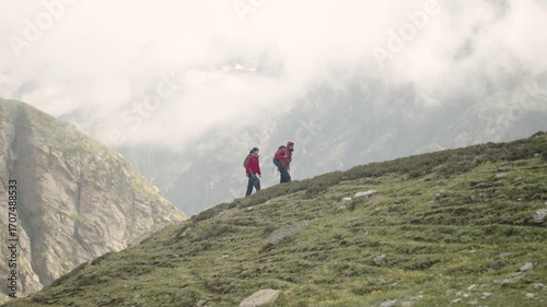 Couple wearing red jackets walking uphill in Hampta Pass mountains, side profile trekking shot symbolizing unity, love, and Himalayan adventure.