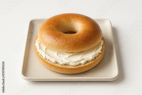 A bagel with cream cheese on a square plate against a white background.