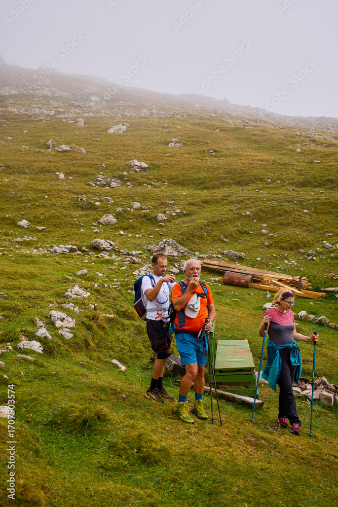 Fototapeta premium a couple with their grandfather walking in the mountains on a cloudy and foggy day.