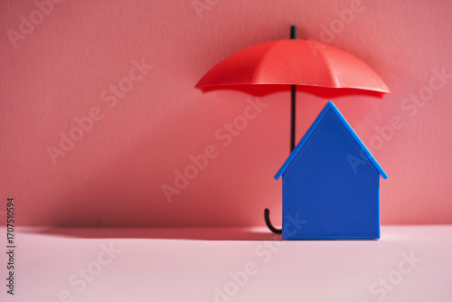 blue house model and toy umbrella against pink background.